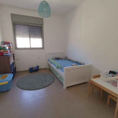 חדר ילדים עם מיטה, מדף צעצועים ושולחן קטן