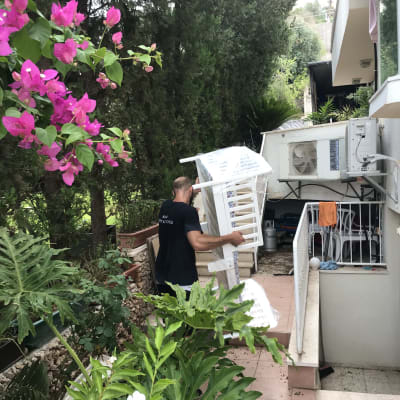 אדם נושא כיסא עטוף בניילון בחצר