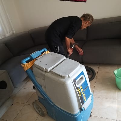 אדם מנקה ספה עם מכונת ניקוי מקצועית ודלי ירוק