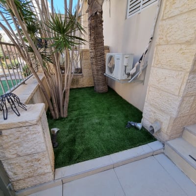 דשא סינתטי עם עצים ודקלים בגינה קטנה