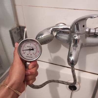 מד לחץ מים מוחזק ליד ברז אמבטיה