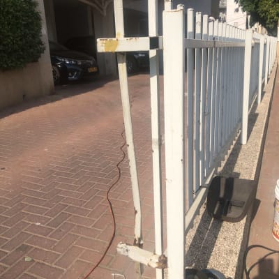 גדר מתכת לבנה עם חלקים חלודים וכלי עבודה על הקרקע