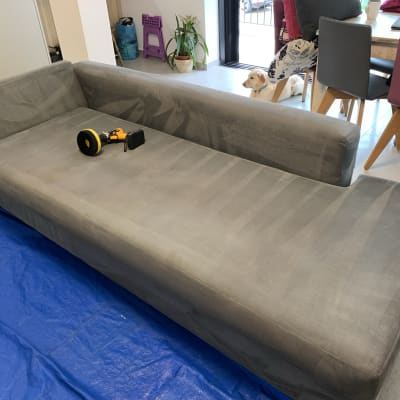 ספה אפורה עם מברשת ניקוי חשמלית על יריעת פלסטיק כחולה