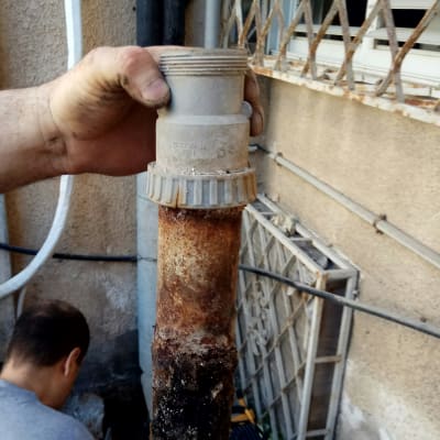 יד מחזיקה צינור חלוד עם לכלוך, אדם עובד ברקע