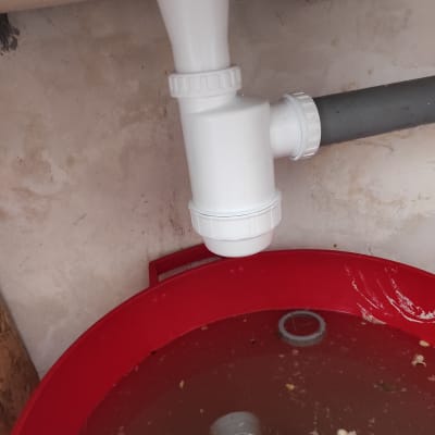 צינור ניקוז לבן מעל דלי אדום עם מים