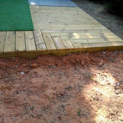 דק עץ חדש ליד דשא סינתטי ואדמה חשופה