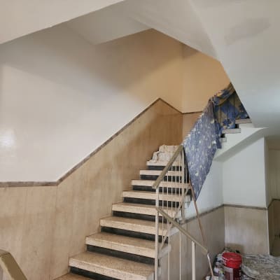 אדם צובע קיר במדרגות עם דלי צבע ומברשת