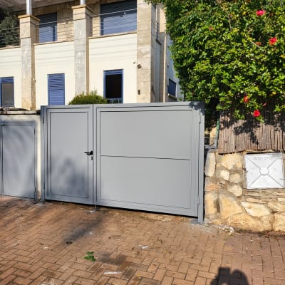 שער מתכת אפור עם ידית על שביל מרוצף