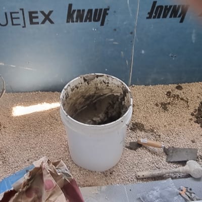 דלי עם מלט, צינורות וכלי עבודה על רצפת חצץ