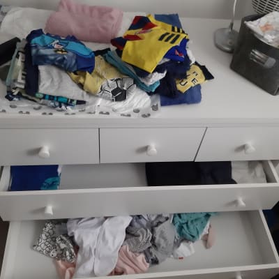 מגירות עם בגדים מקופלים ומפוזרים על שידה לבנה