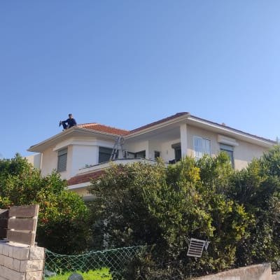 אדם יושב על גג רעפים עם סולם בצד