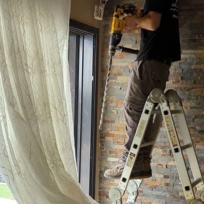 חשמלאי על סולם עם מקדחה חשמלית ביד