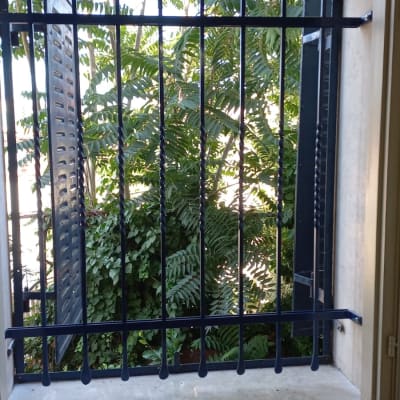 סורגי מתכת כחולים בחלון פתוח עם צמחייה בחוץ