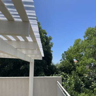 פרגולה מעץ עם גג פלסטיק שקוף ליד עצים ירוקים