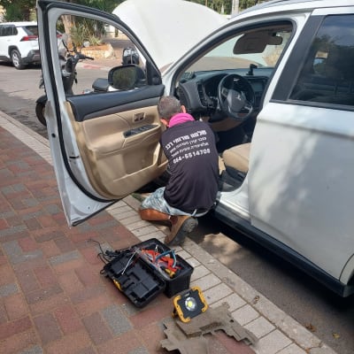 אדם מתקן רכב עם כלים פתוחים על המדרכה