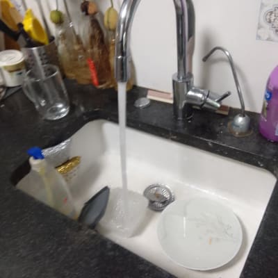 ברז מים זורמים בכיור מטבח עם כלים וסבון.