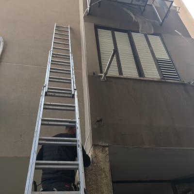 טכנאי מטפס על סולם לתיקון מזגן חיצוני
