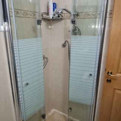 מקלחון עם דלתות זכוכית ומדף עם מוצרי רחצה