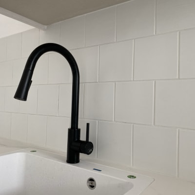 ברז שחור מותקן על כיור לבן עם אריחים לבנים