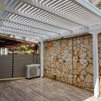 פרגולה לבנה מעל רצפת דק ליד קיר אבן