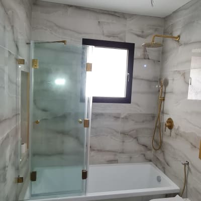 מקלחת עם דלת זכוכית וברז זהב על קיר שיש