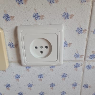 שקע חשמל לבן על קיר עם אריחים פרחוניים