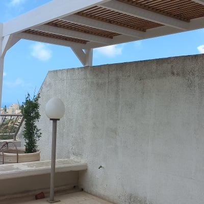 פרגולה מעץ לבן על מרפסת עם קיר לבן