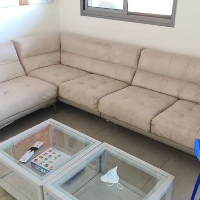 ספה בהירה עם כתמים קלים, שולחן זכוכית עם מסכה.