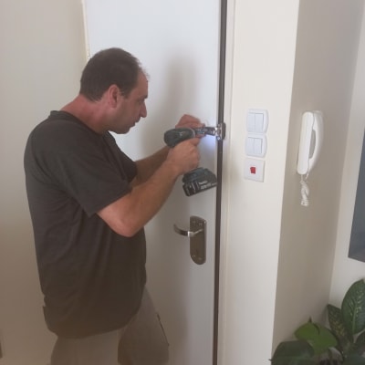 אדם מתקין ציר לדלת בעזרת מברגה חשמלית