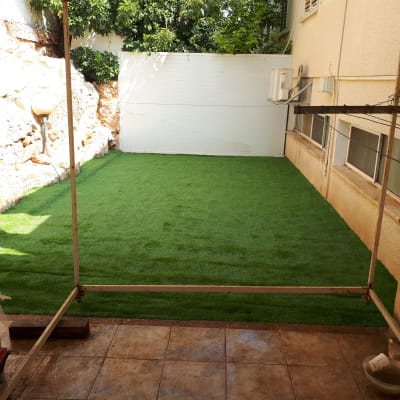 דשא סינתטי בחצר קטנה עם קיר אבן