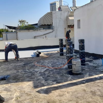 עובדים אוטמים גג עם יריעות ביטומניות ומבער גז