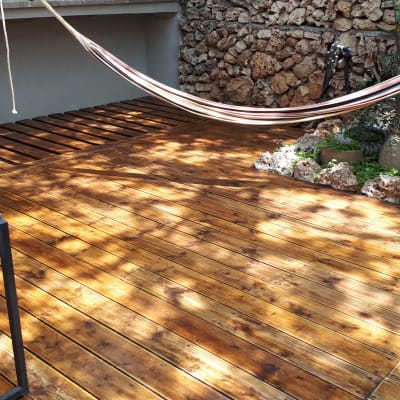 דק עץ עם ערסל בגינה מוקפת צמחייה ואבנים