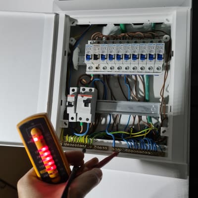 לוח חשמל פתוח עם חוטים ומד מתח ביד חשמלאי