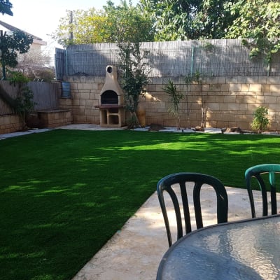 דשא סינתטי בגינה עם עצים ושיחים מסביב