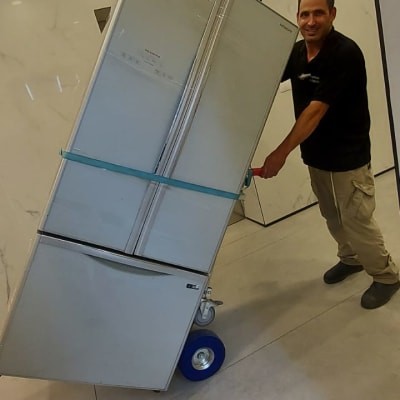 אדם מזיז מקרר על עגלת משא עם גלגלים כחולים