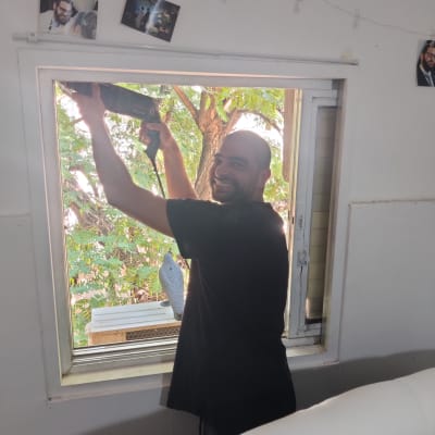 אדם מחזיק מקדחה ליד חלון פתוח