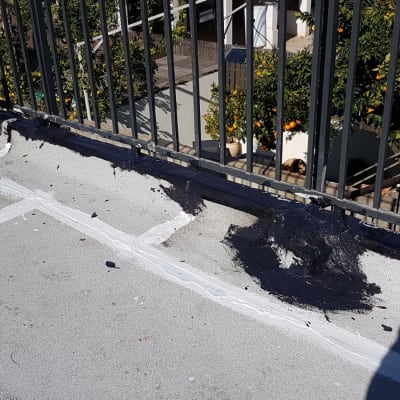 אדם מורח חומר איטום שחור על גג ליד מעקה.