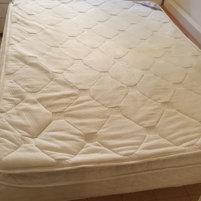 מזרן עם כתמים על רצפה מרוצפת, שואב אבק בצד