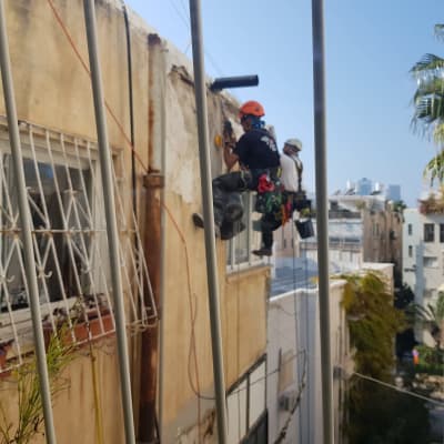 שני פועלים על חבלים מתקנים קיר חיצוני של בניין