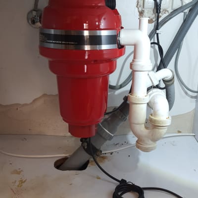 מטחנת אשפה אדומה מותקנת מתחת לכיור עם צינורות חיבור