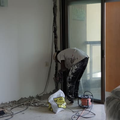 עובד קודח בקיר עם מקדחה חשמלית, כבלים על הרצפה