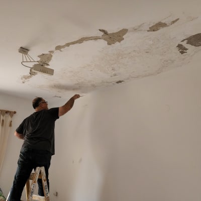 אדם צובע תקרה עם קילופים בעזרת מברשת.