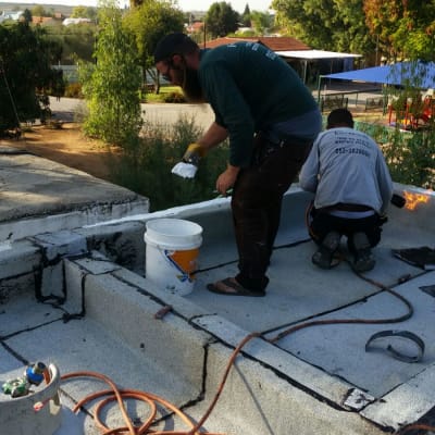 שני אנשים עובדים על איטום גג עם חומר לבן ודלי