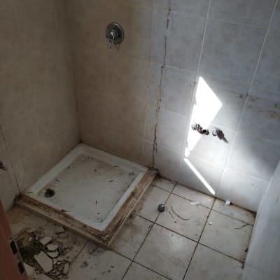 מקלחת ישנה עם אריחים שבורים ופסולת על הרצפה