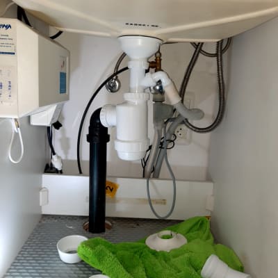 צנרת פלסטיק לבנה מתחת לכיור עם מגבת ירוקה