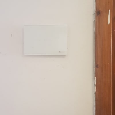 תרמוסטט לבן מותקן על קיר ליד מסגרת עץ