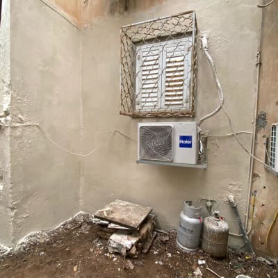 קיר עם מזגן, בלוני גז, דלי צבע, ערימת אריחים