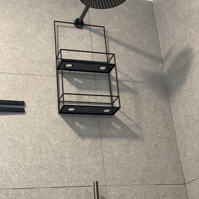 ראש מקלחת ומדף מתכת על קיר אריחים אפור