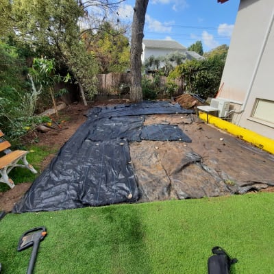 יריעות פלסטיק שחורות על הקרקע בגינה עם כלי גינון