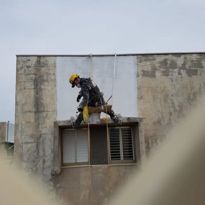 אדם עם קסדה צובע קיר חיצוני בעזרת חבלים